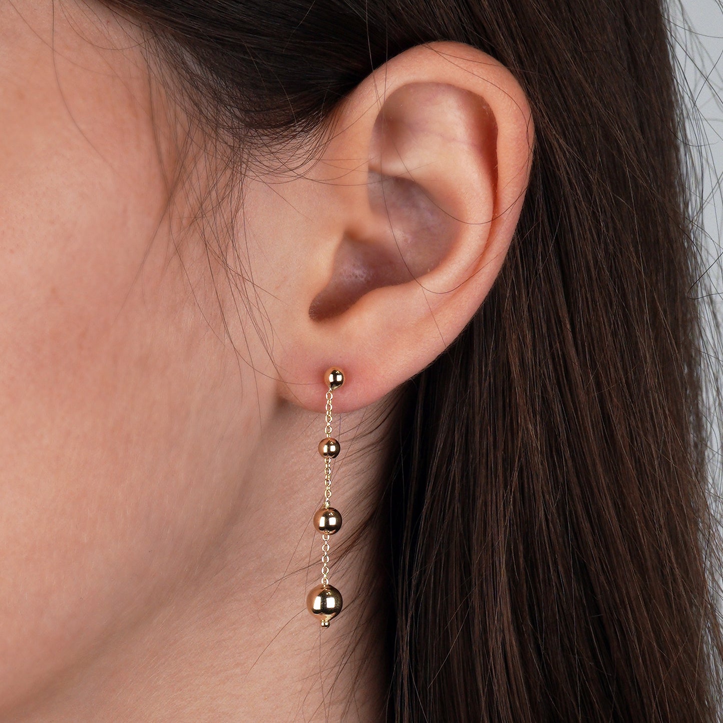 Złote kolczyki z drobnymi kulkami na cienkim łańcuszku – elegancka i delikatna biżuteria.