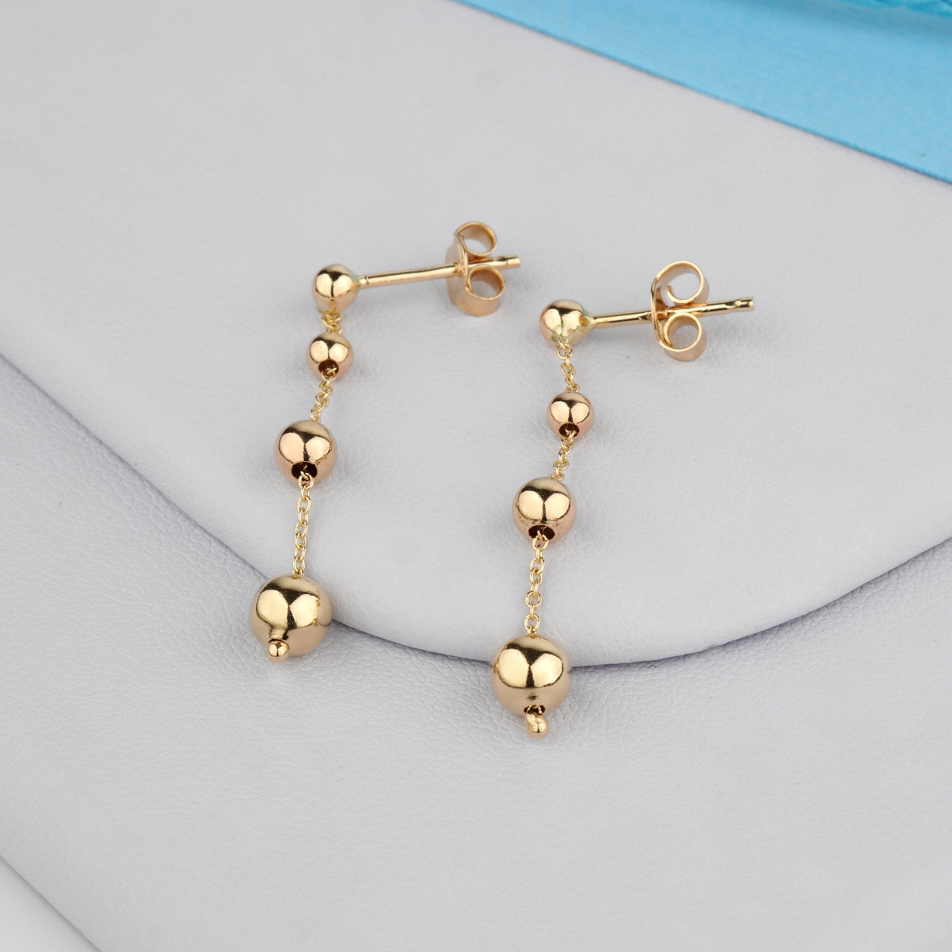 Złote kolczyki z drobnymi kulkami na cienkim łańcuszku – elegancka i delikatna biżuteria.