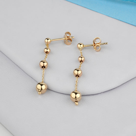 Złote kolczyki z drobnymi kulkami na cienkim łańcuszku – elegancka i delikatna biżuteria.