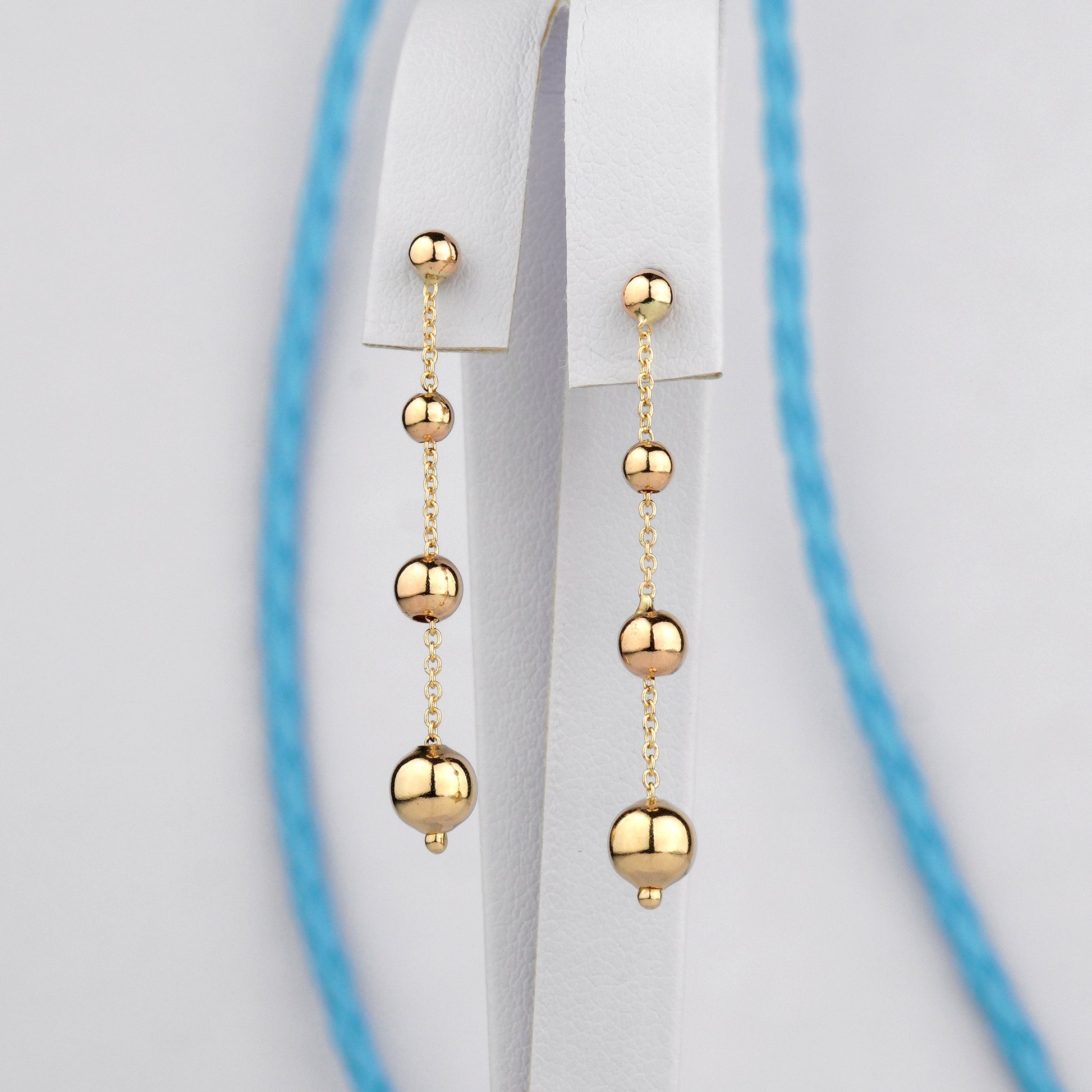 Złote kolczyki z drobnymi kulkami na cienkim łańcuszku – elegancka i delikatna biżuteria.