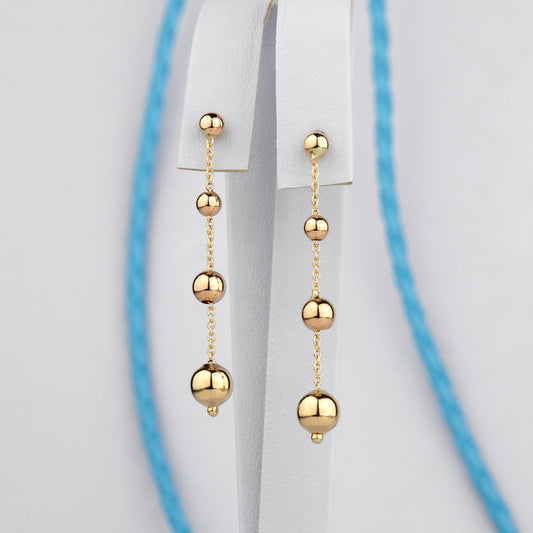 Złote kolczyki z drobnymi kulkami na cienkim łańcuszku – elegancka i delikatna biżuteria.